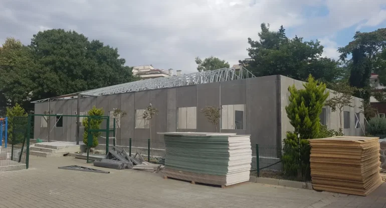 MEB standartlarına uygun, çelik makaslı prefabrik okul binası montaj süreci ve derslik panelleri saha stok alanı.