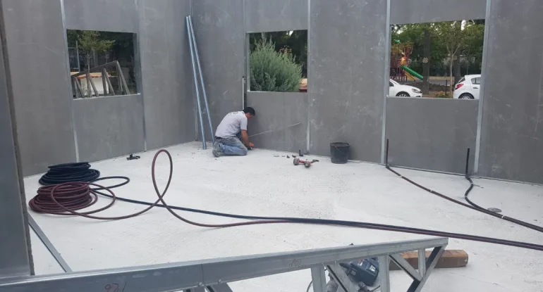 Hafif çelik konstrüksiyonlu prefabrik okul derslik montajı ve iç mekan yalıtımlı panel yerleşimi.